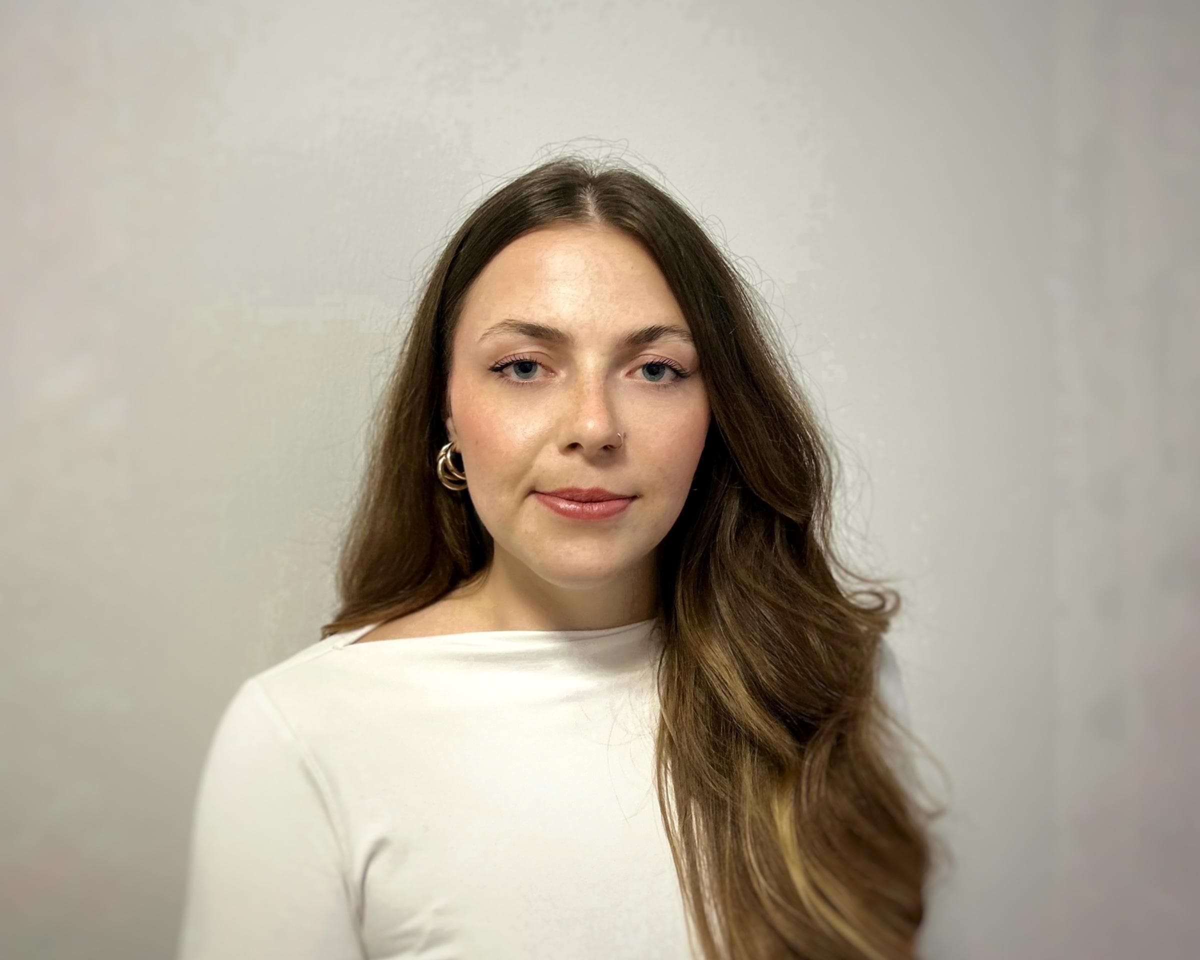 Leonie Schlegel ist SEO Managerin bei Hiscox Deutschland. Sie hat lange braune Haare, trägt goldene Ohrringe, ein weißes Shirt und lächelt in die Kamera.