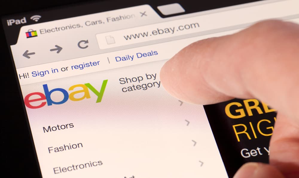 Finger zeigt auf die geöffnete Startseite von eBay im Browser auf den Button "Shop by category"