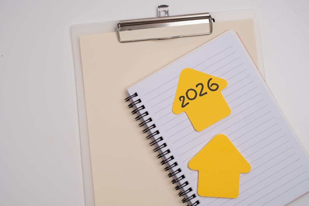 Spiralblock mit zwei gelben, pfeilförmigen Haftnotizen, eine davon mit der Aufschrift „2026“, auf einer linierten Seite. Unter dem Notizbuch befindet sich ein Klemmbrett.