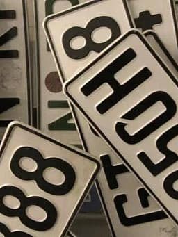 Ein Stapel von Fahrzeugkennzeichen, die sich überlappen. Ein auffälliges Kennzeichen in der Mitte trägt die Aufschrift "P25OSH", ein weiteres sichtbares Kennzeichen lautet "888".