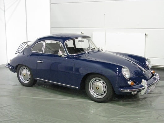 Ein dunkelblauer Oldtimer-Sportwagen Porsche 356 SC mit schlankem Design steht in einer Garage. Er hat eine runde Karosserie, Chromdetails und einen Gepäckträger am Heck.