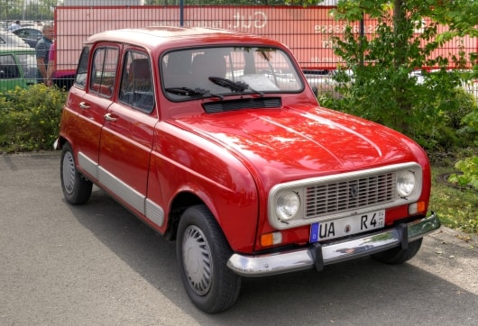 Ein alter roter Renault R4 GLT steht an einem sonnigen Tag im Freien. Es hat ein kantiges Design, Chromdetails und einen klassischen Look, der Nostalgie und Charme ausstrahlt.
