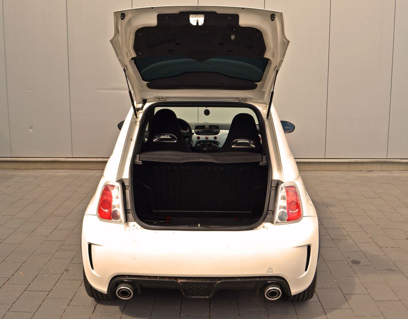 Weißer Abarth 500 steht parkend vor einer grauen Wand mit Blick in den offenen Kofferraum.