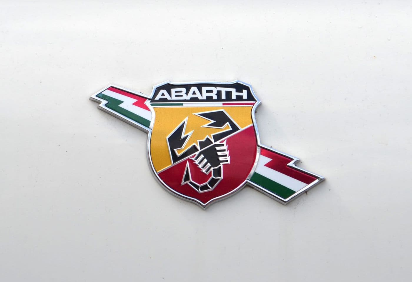 Das Markenlogo des Fiat Abarth 500 - ein schwarzer Skorpion auf dem rot gelben Siegeln. Im Hintergrund der grün, weiß, rote Blitz (Italien).