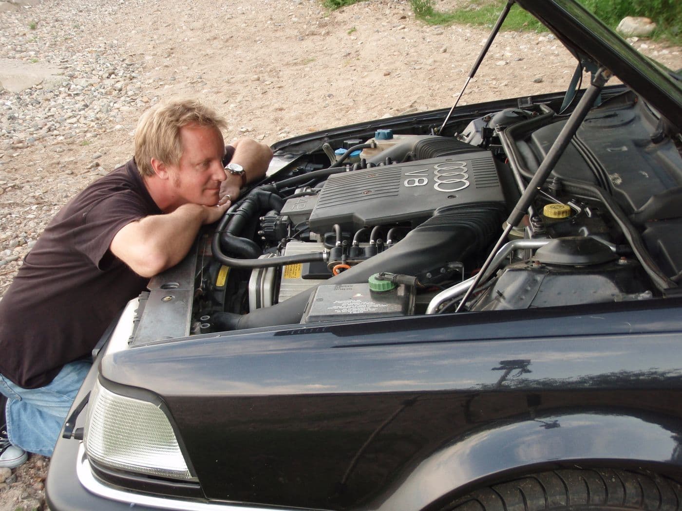 Jens Tanz blickt in den Motorraum des schwarzen Audi v8 auf den Motor.