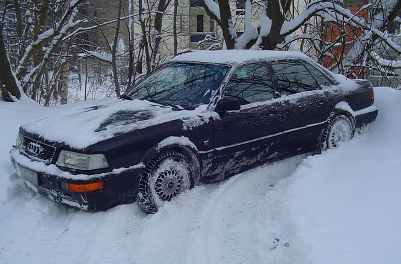 Der Audi v8 4,2 Quattro geparkt im Tiefschnee auf einer zugeschneiten Straße neben Bäumen.