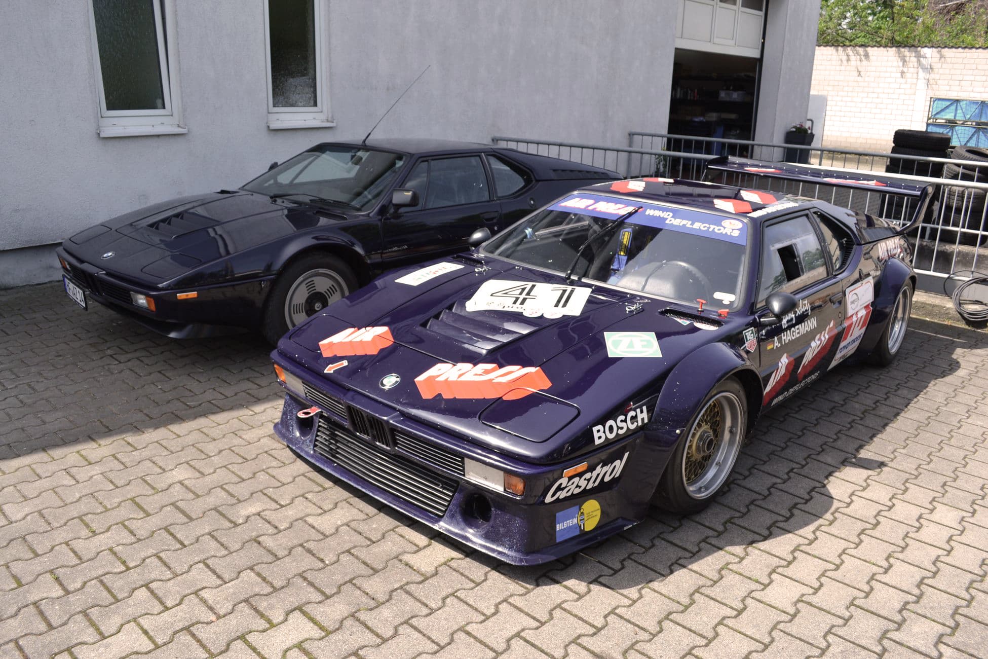 Auf einer Ziegelstein-Auffahrt sind zwei Oldtimer geparkt, davon ist einer der BMW M1.