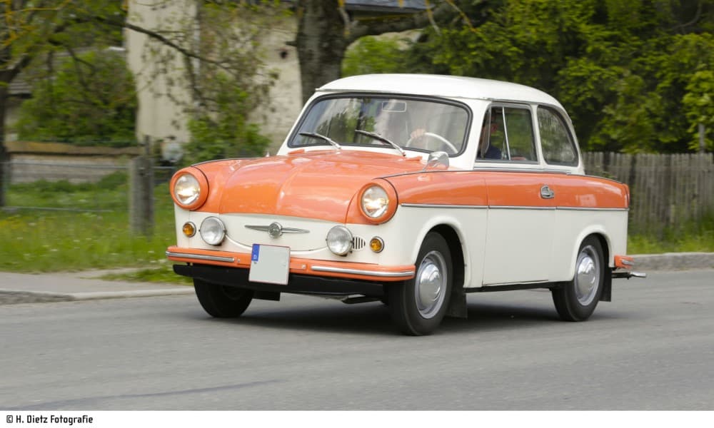 Der Oldtimer Trabant 600 in Orange und Weiß fährt die Straße entlang.