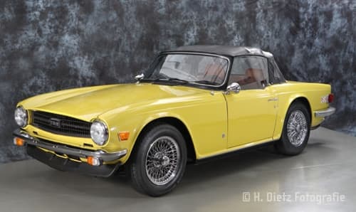 Ein gelber Triumph TR6 steht in einem Studio geparkt und strahlt Eleganz und Stil aus.