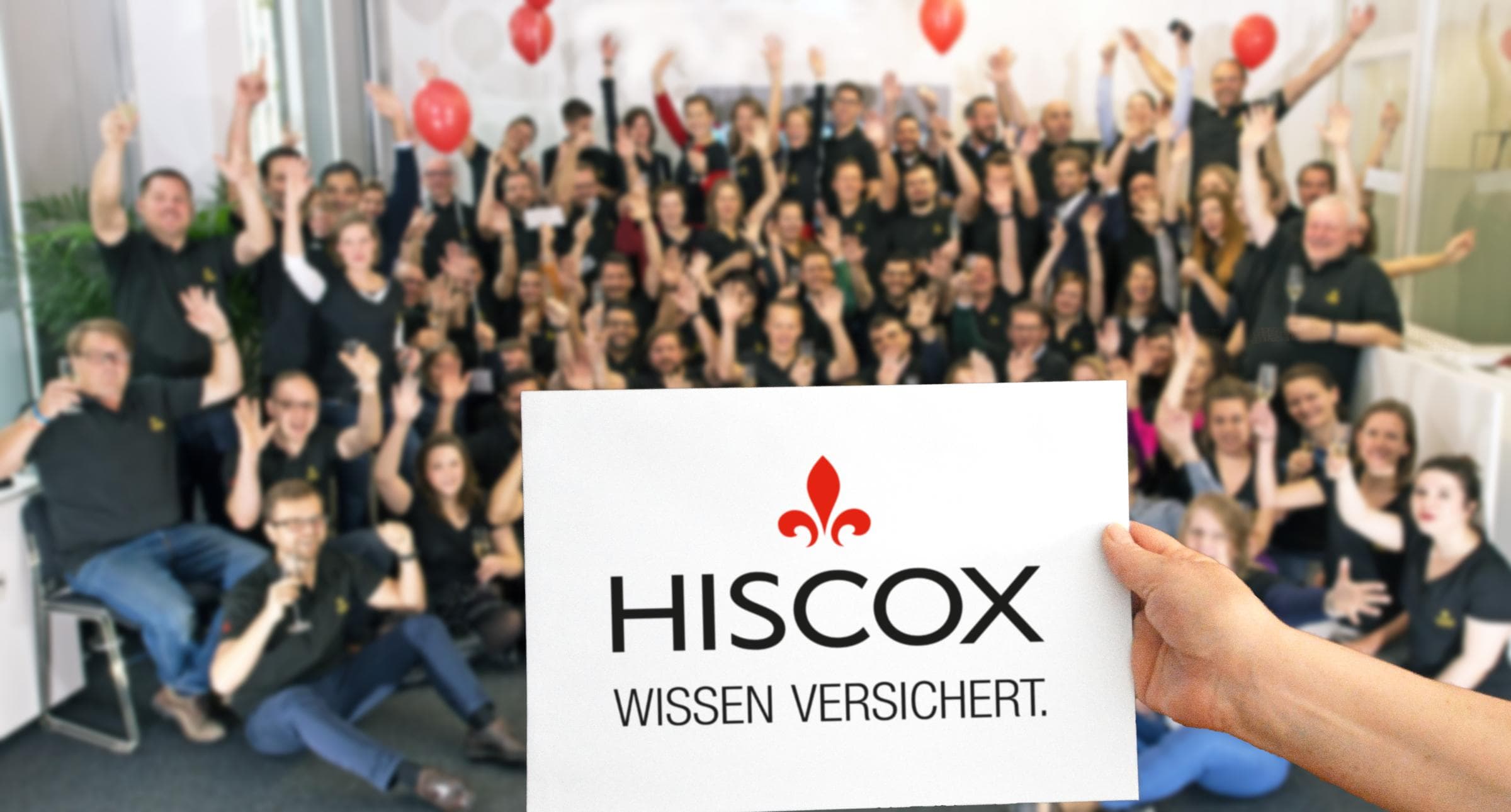 Das Mitarbeiter-Team von Hiscox Deutschland jubelt. Im Vordergrund sieht man das Hiscox Logo.