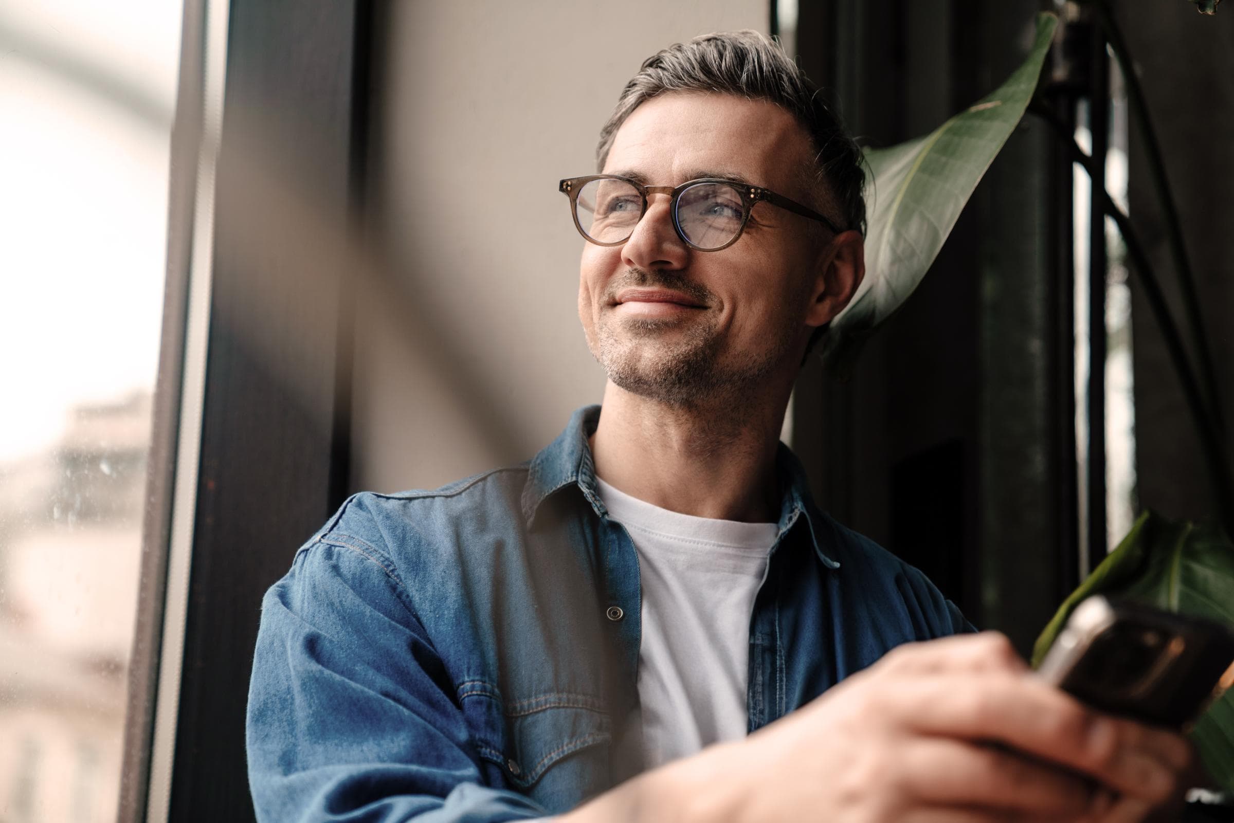 Ein Mann mit einem Smartphone in der Hand blickt aus dem Fenster