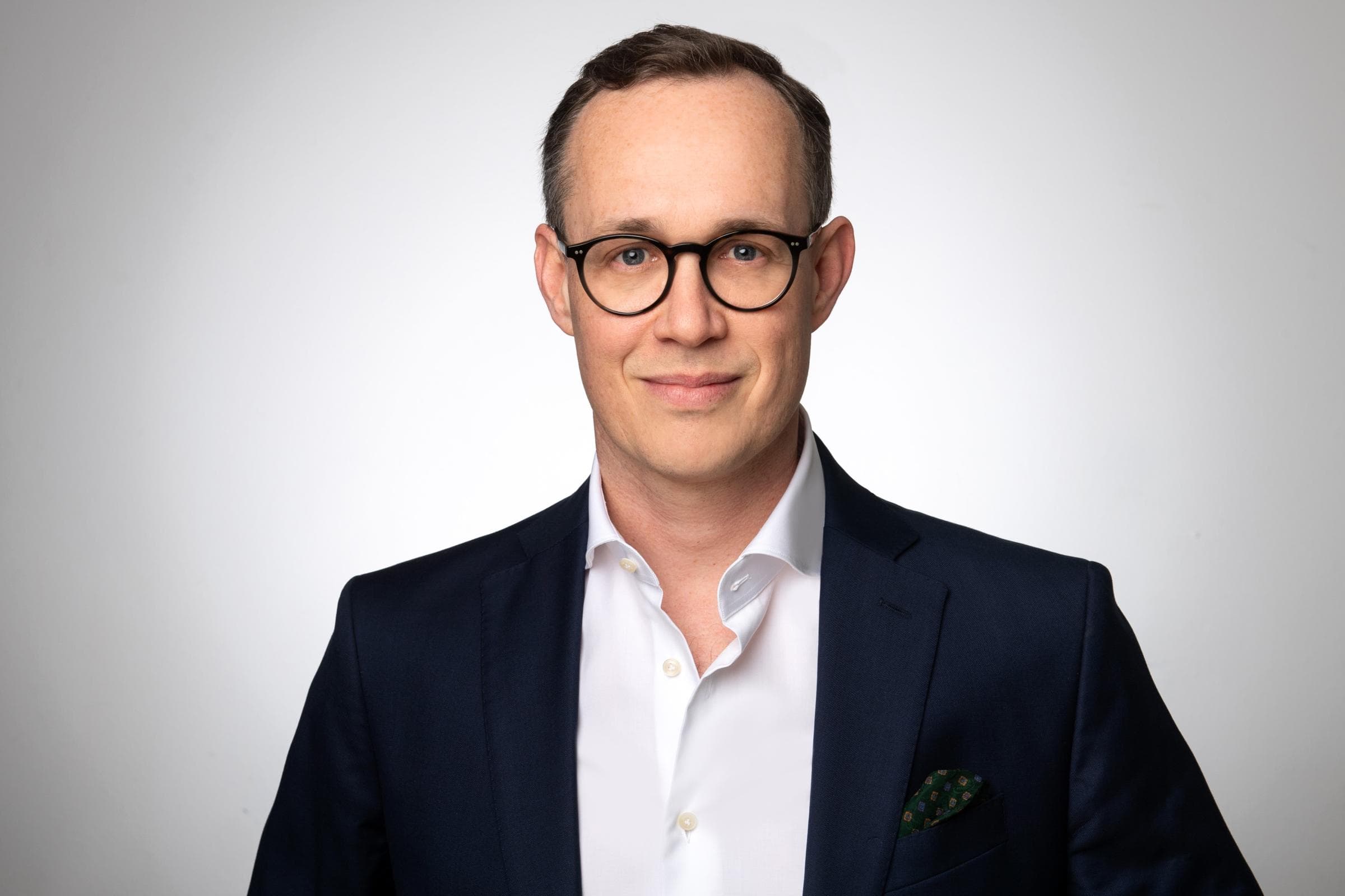 Maximilian Heidbrink, Interim Head of Claims Germany, steht in Anzug, Hemd und schwarzer Brille vor einer weißen Wand.