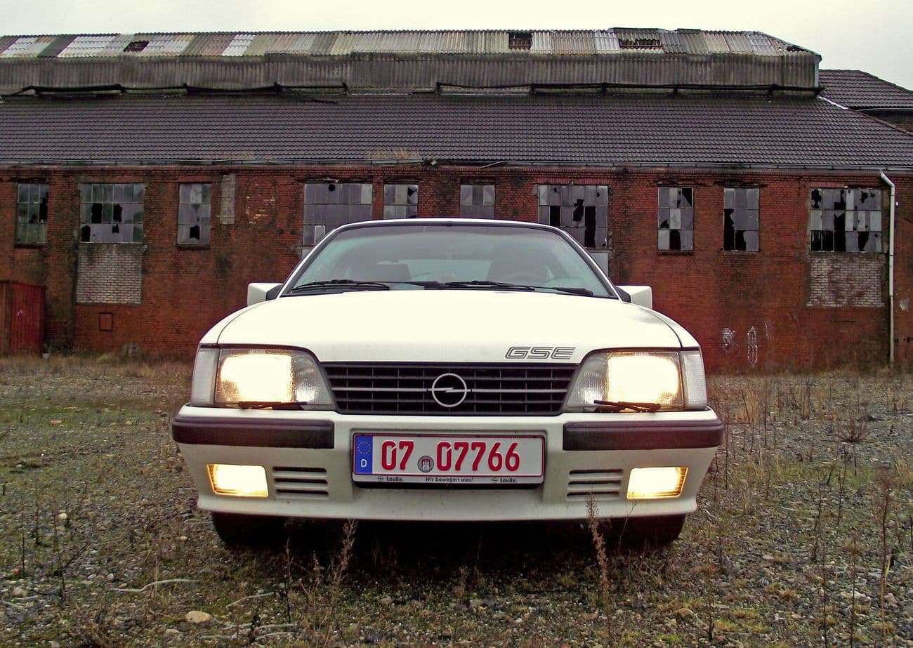 Opel Monza GSE in weiß geparkt vor einem Backsteinhaus in Frontansicht.