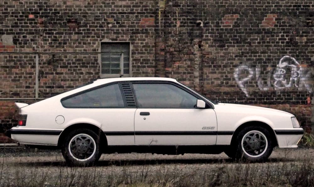 Weißer Opel Monza GSE parkt vor einer Backsteinwand mit Graffiti von Jens Tanz.