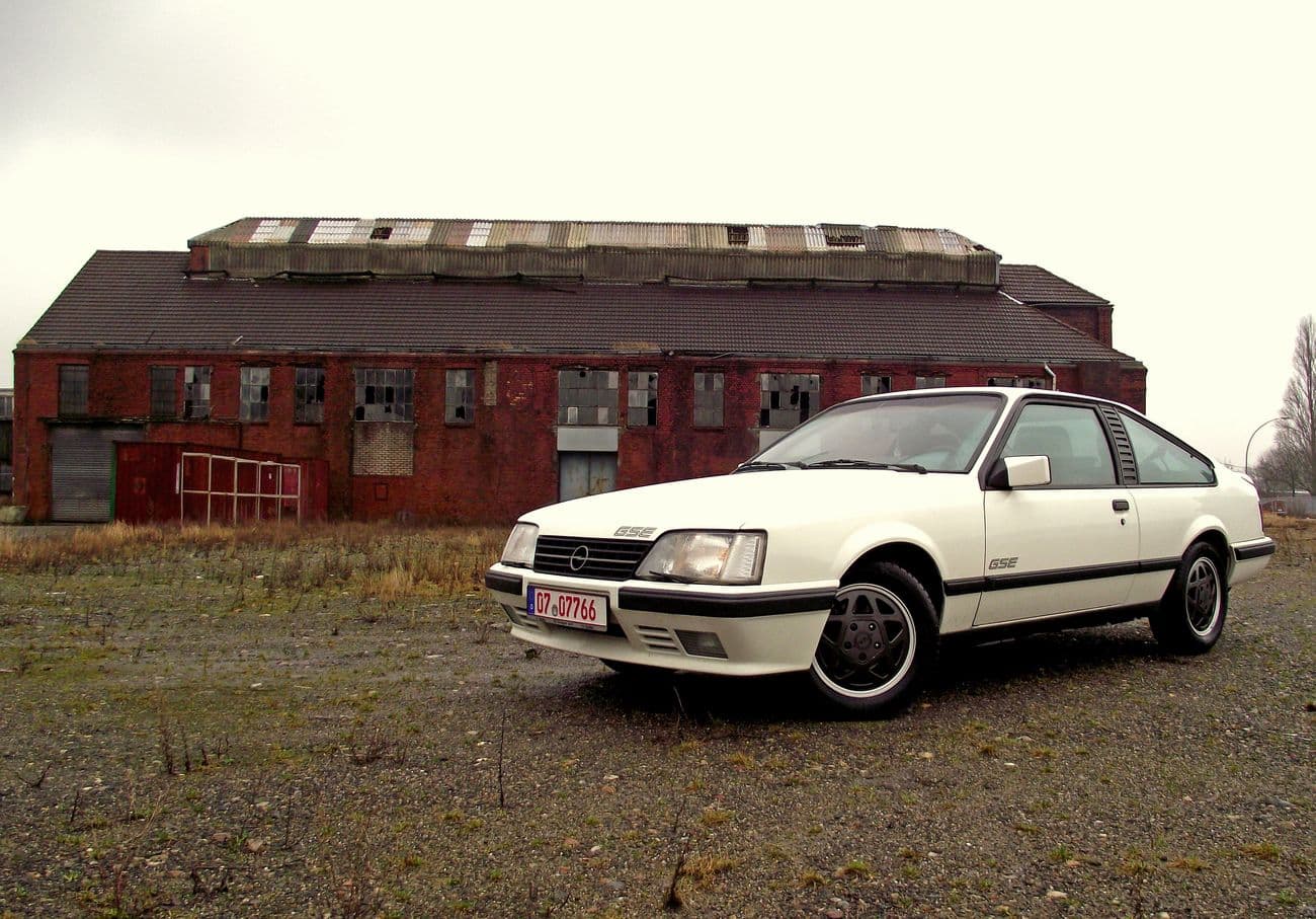 Parkender weißer Opel Monza GSE in der Seitenansicht vor einem roten Backsteinhaus.