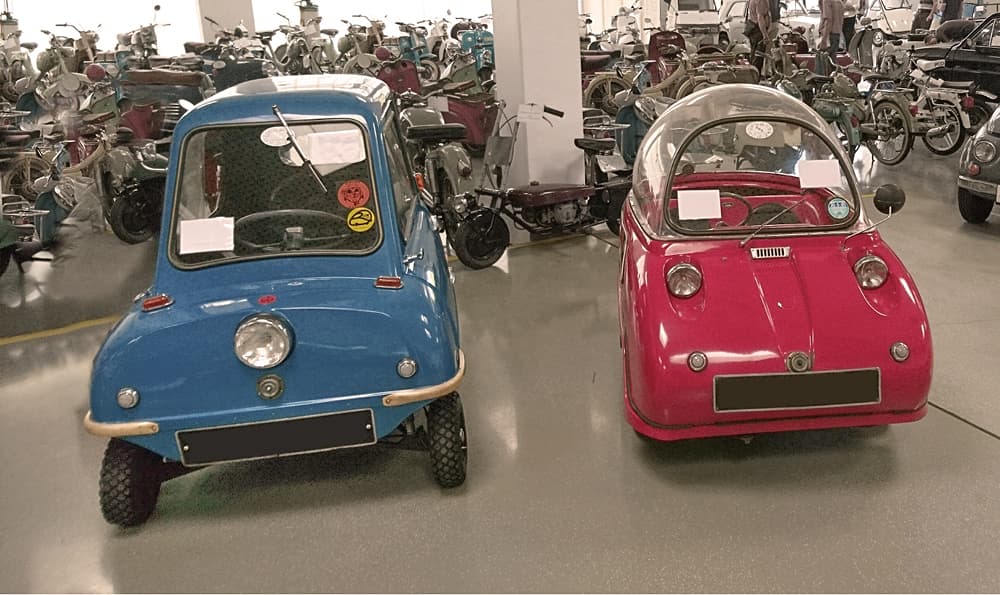 Blauer Peel P50, das kleinste Auto der Welt, parken in einem Oldtimer-Museum neben einem roten Variante Peel Trident