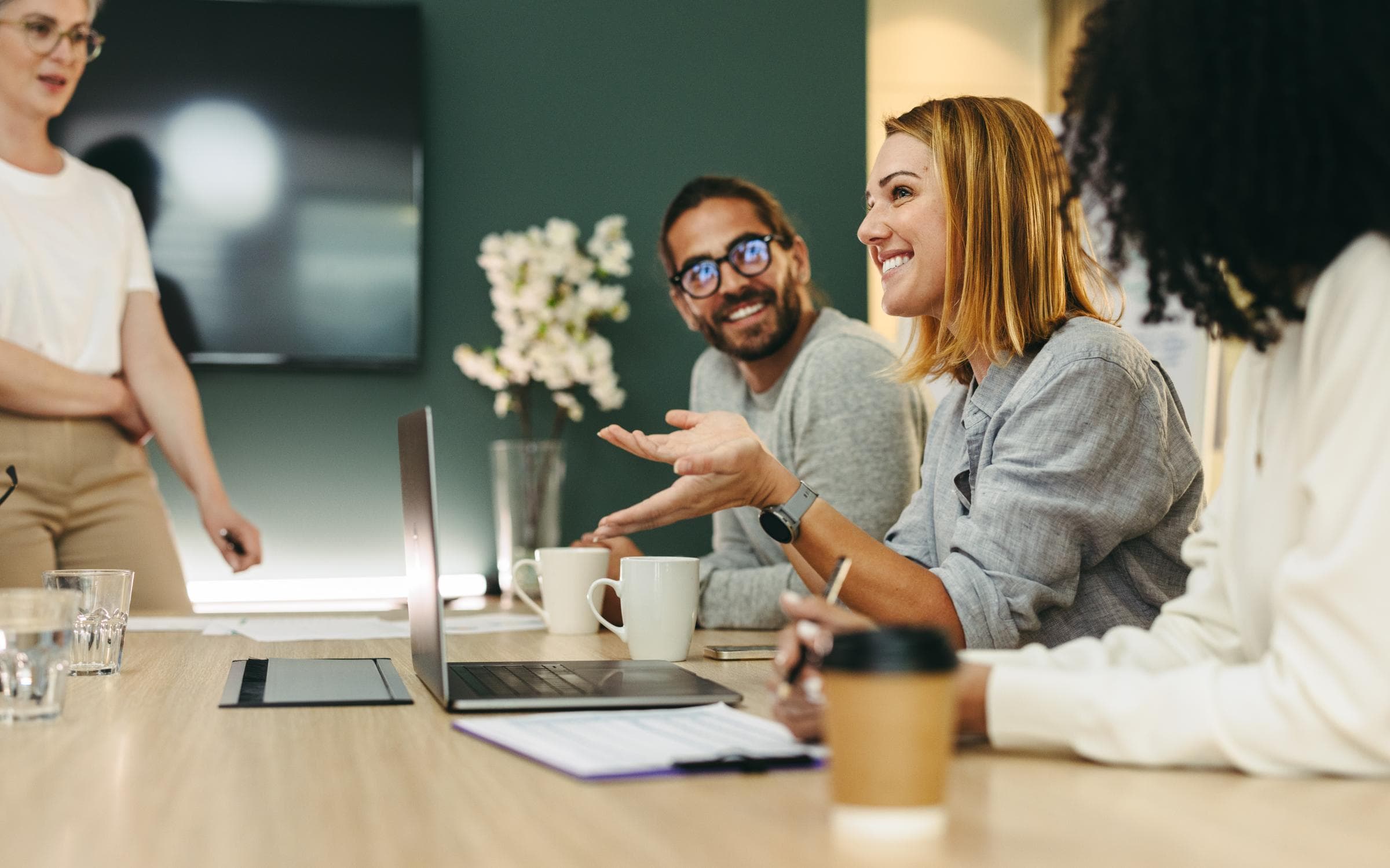 Vier HR Mitarbeiter sitzen um einen Meetingtisch in einem Meetingraum und reden miteinander. auf dem Tisch steht ein Laptop und Kaffeebecher.