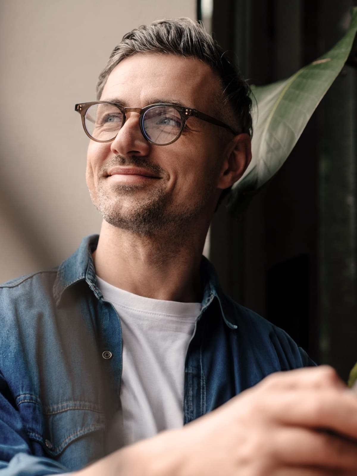 Mann mit Brille, Jeanshemd und weißem T-Shirt lächelt. Es handelt sich dabei um einen jungen Unternehmer.