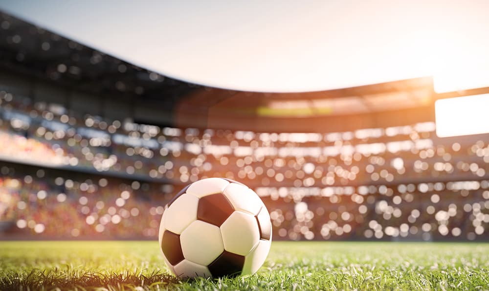 Fußball liegt auf grünem Rasen in einem vollen Fußballstadion mit Zuschauern bei Sonnenschein