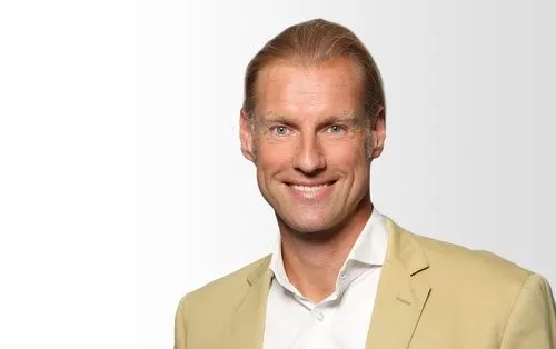 Dirk Koerbel, Branch Office Manager von Hiscox Stuttgart, lächelt in die Kamera. Er trägt ein weißes Hemd, beigen Blazer und hat helle Haare.
