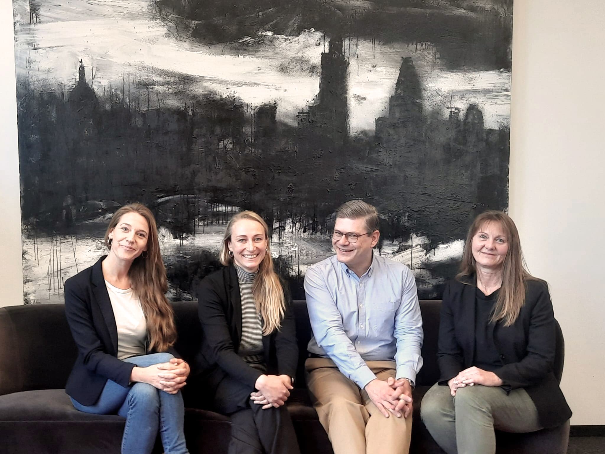 Das Hiscox HR-Team Deutschland sitzt auf einem Sofa im Büro vor einem Gemälde.
