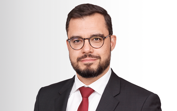 Markus Niederreiner, der CEO von Hiscox Deutschland, trägt einen schwarzen Anzug, schwarze Brille, ein weißes Hemd und eine rote Kravatte.